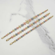 Three gold Fiori hibiscus flower link bracelets laid diagonally on white marble