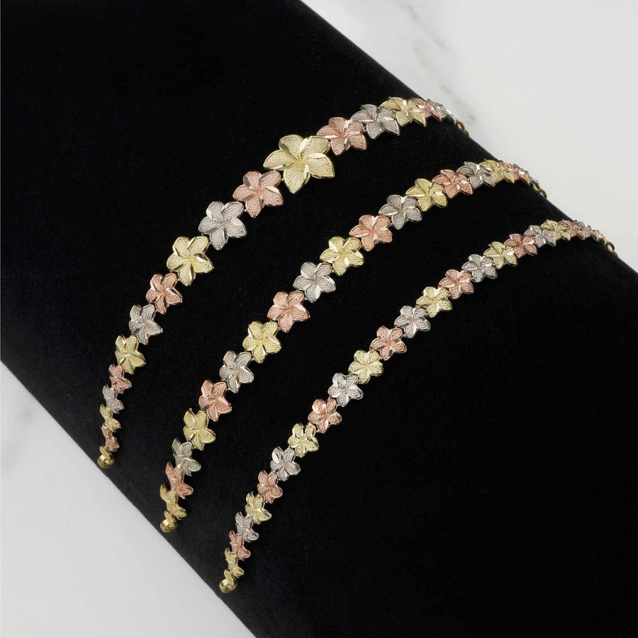 Three gold hibiscus flower bracelets in varying widths displayed on a black surface.