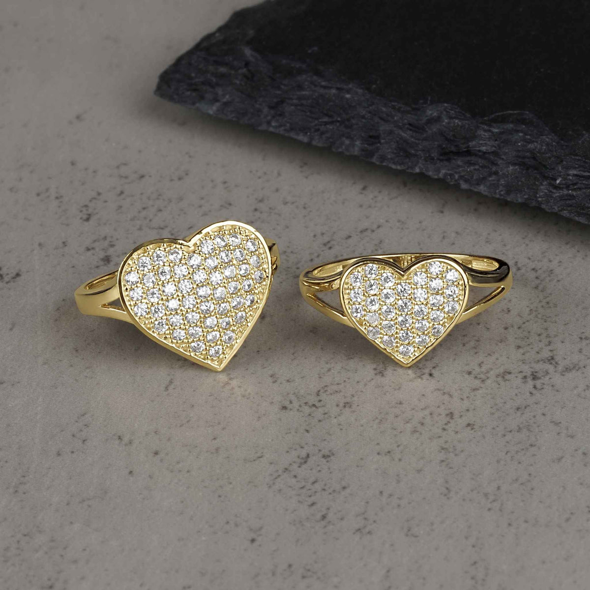 Two 10k-14k gold heart-shaped rings encrusted with white cubic zirconia stones on stone.