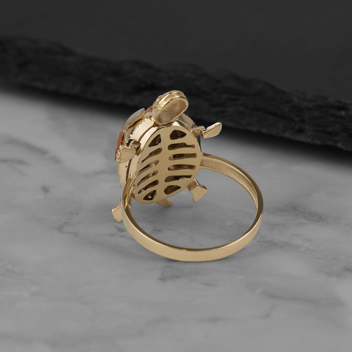 Underside view of a gold turtle locket ring showing its intricate ribbed pattern.