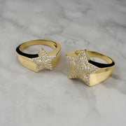 Two gold star-shaped rings encrusted with shimmering cubic zirconia on marble.