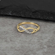 Gold infinity loop ring accented with cubic zirconia stones on a gray stone surface