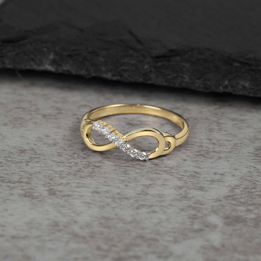 Gold infinity loop ring accented with cubic zirconia stones on a gray stone surface