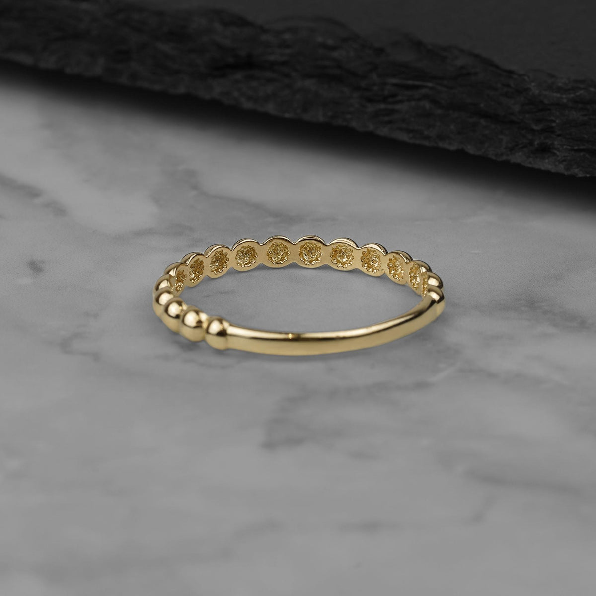 Elegant view of a thin beaded yellow gold band on a neutral surface.