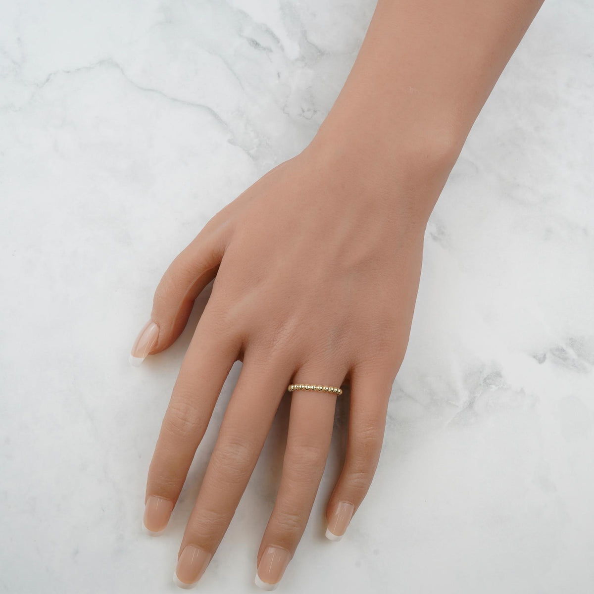 Overhead view of a hand wearing a delicate yellow gold beaded thin band ring.
