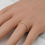 Close-up of a delicate yellow gold beaded thin band ring worn on a finger.