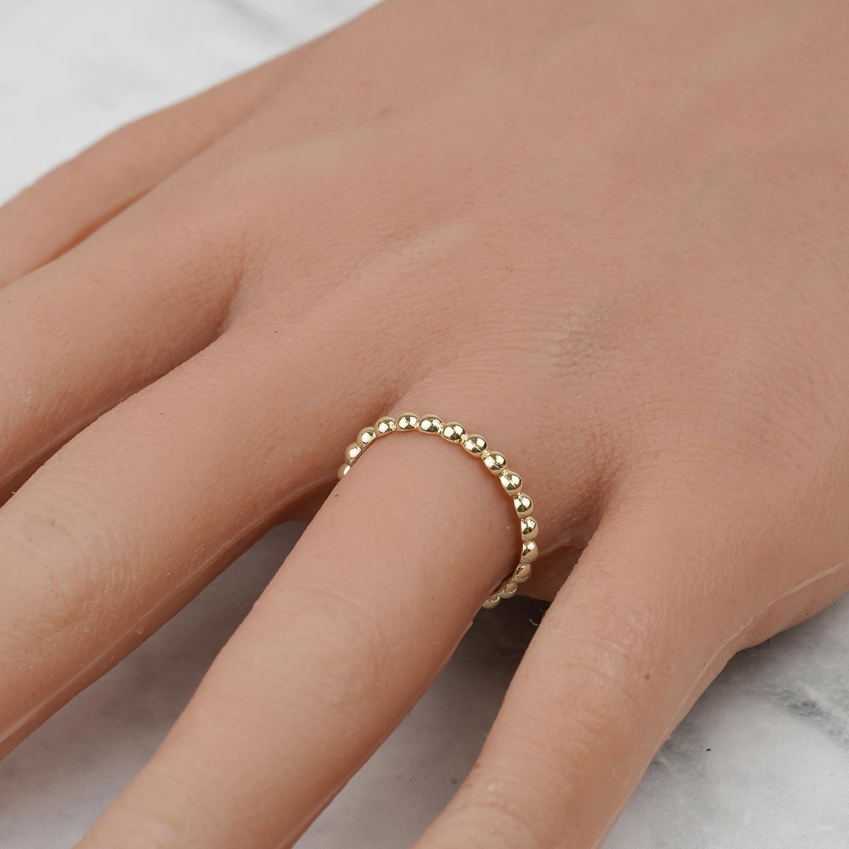 Close-up of a delicate yellow gold beaded thin band ring worn on a finger.