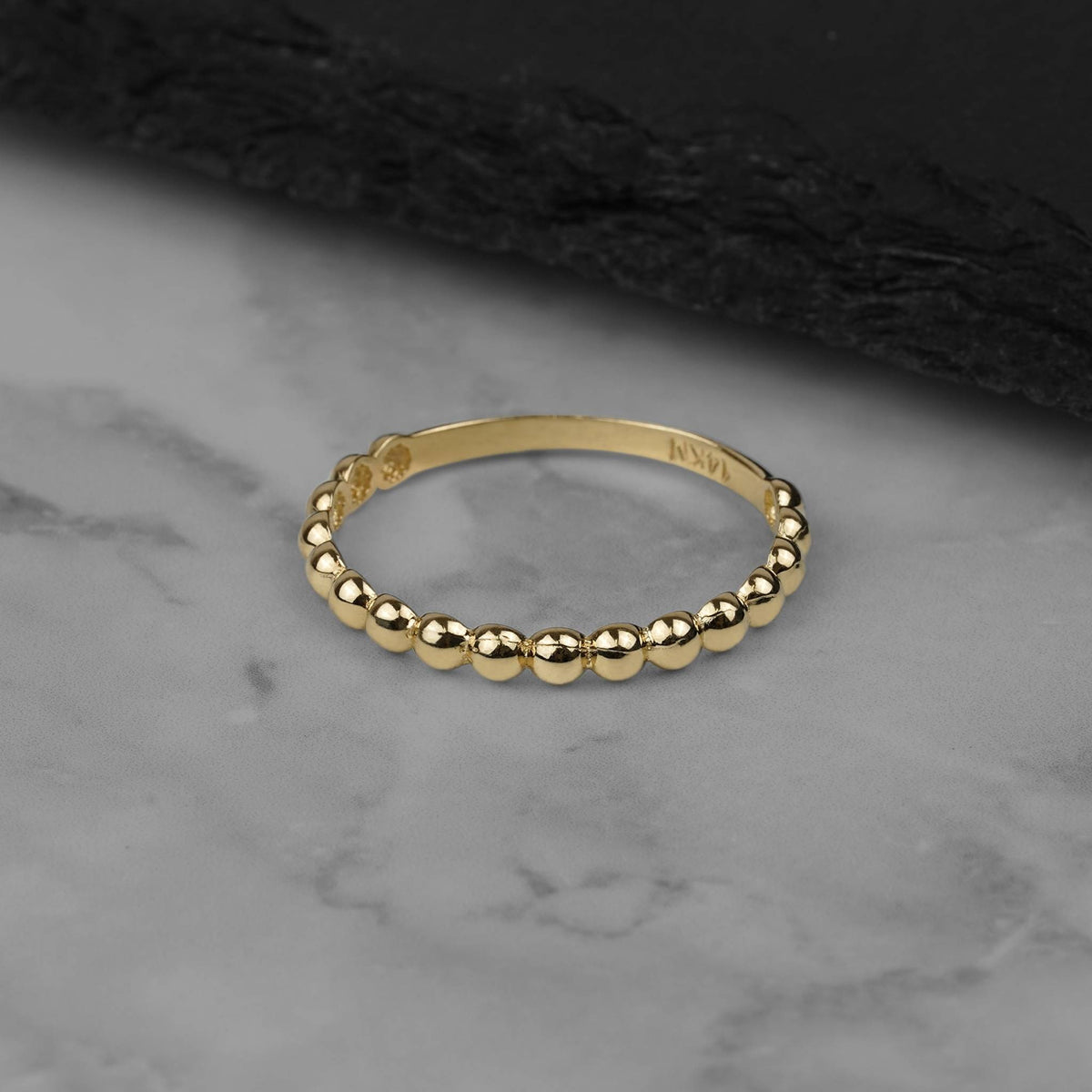 Delicate yellow gold bead-textured thin band ring resting on a marble surface.