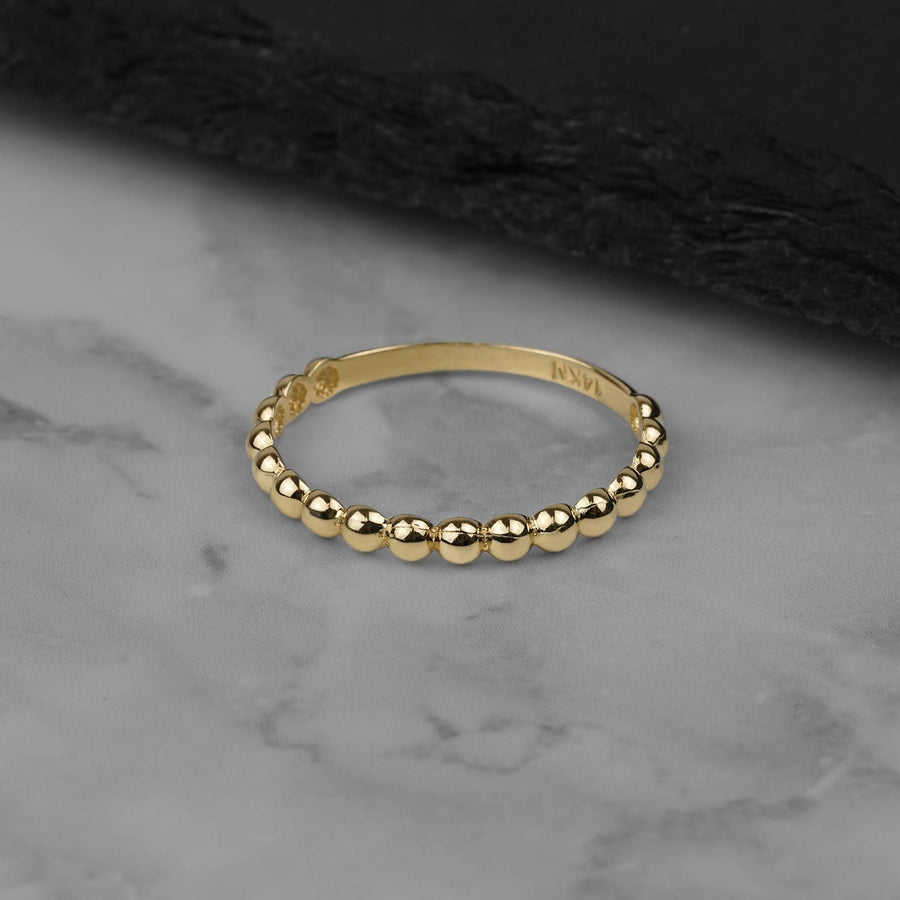 Delicate yellow gold bead-textured thin band ring resting on a marble surface.