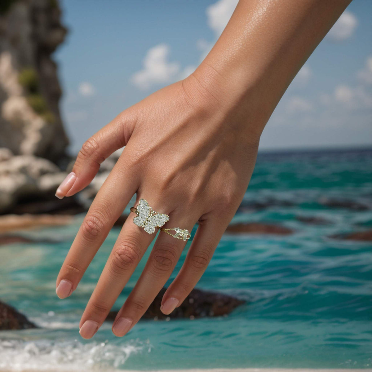 Model wearing a sparkling gold butterfly statement ring outdoors against a scenic ocean backdrop.