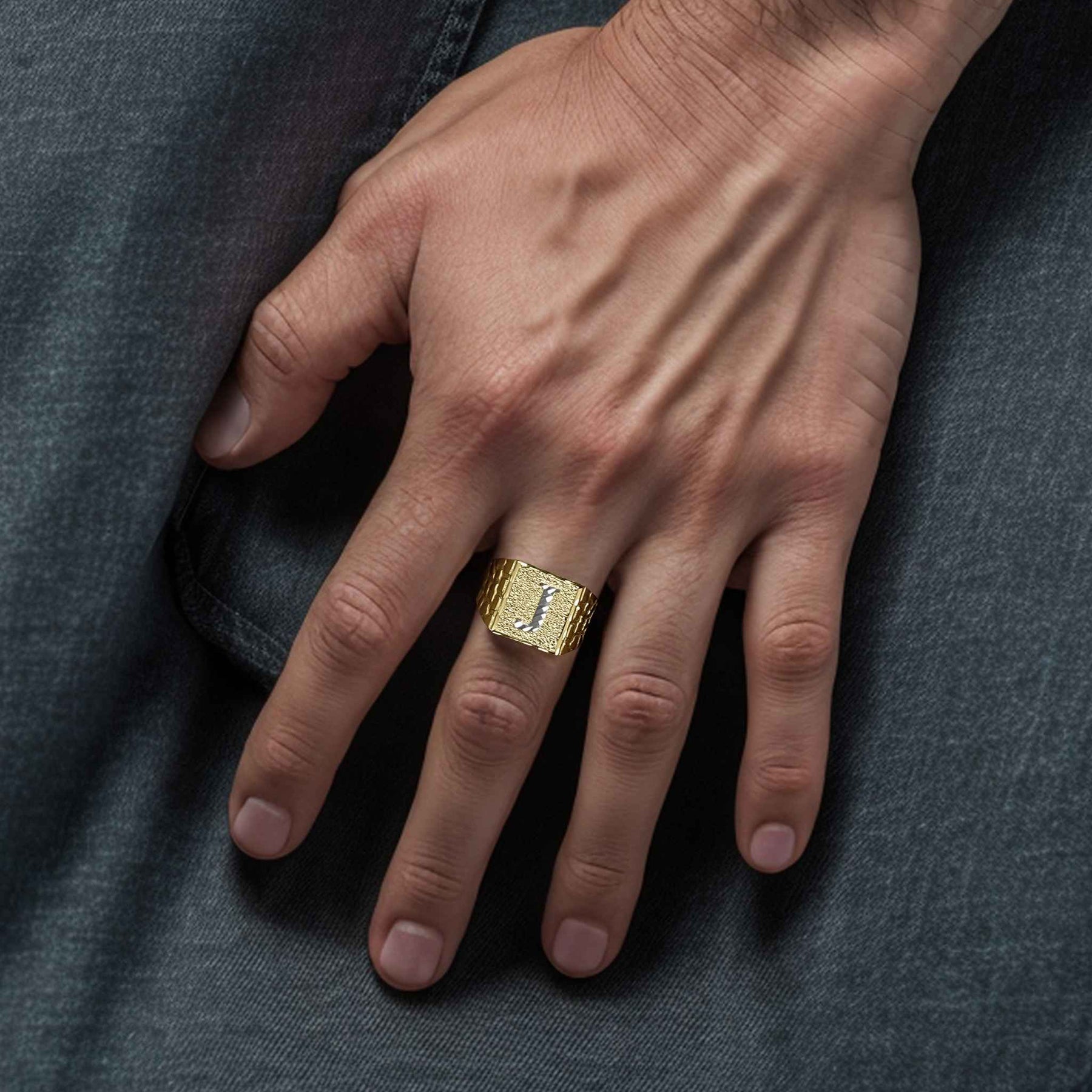 Model wearing a gold square nugget initial J ring on a denim fabric background.