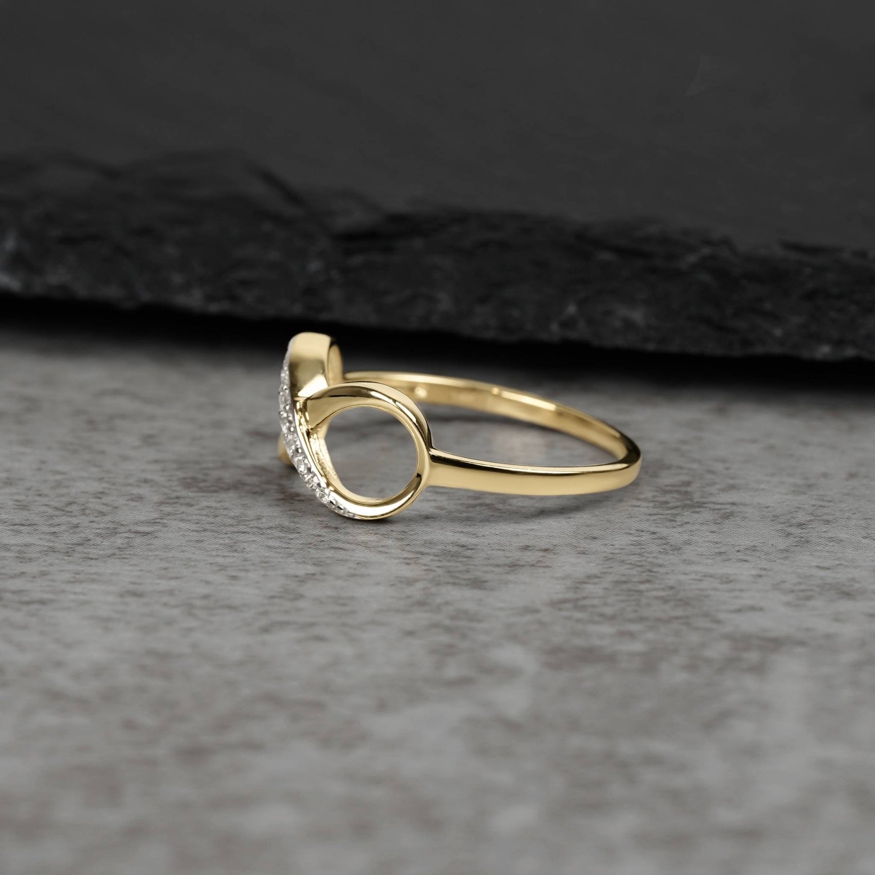 Polished gold infinity band featuring sparkling cubic zirconia crystals on a textured gray surface.
