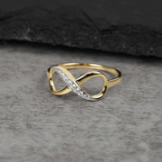Solid yellow gold Meir infinity ring with cubic zirconia stones on gray stone surface.