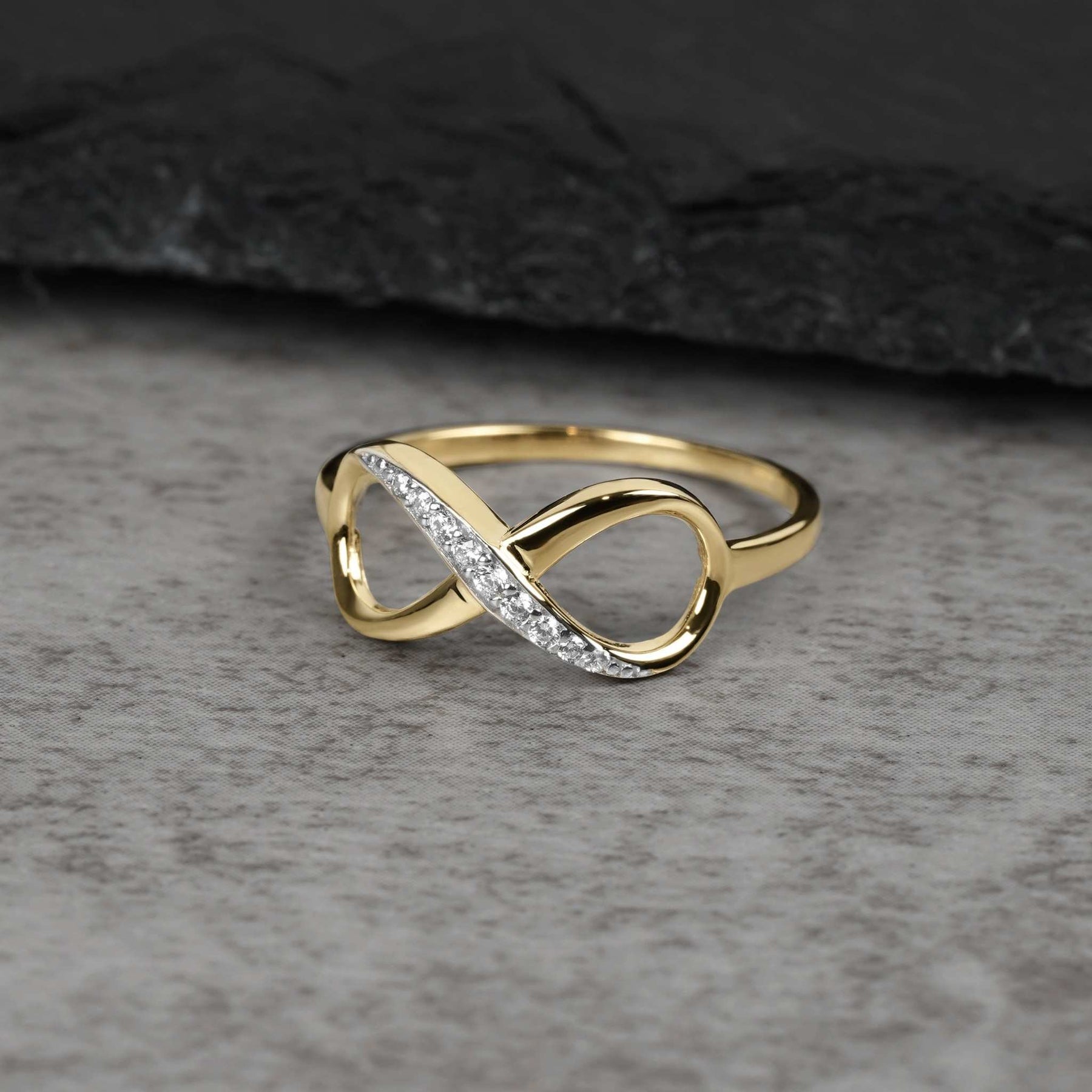 Solid yellow gold Meir infinity ring with cubic zirconia stones on gray stone surface.