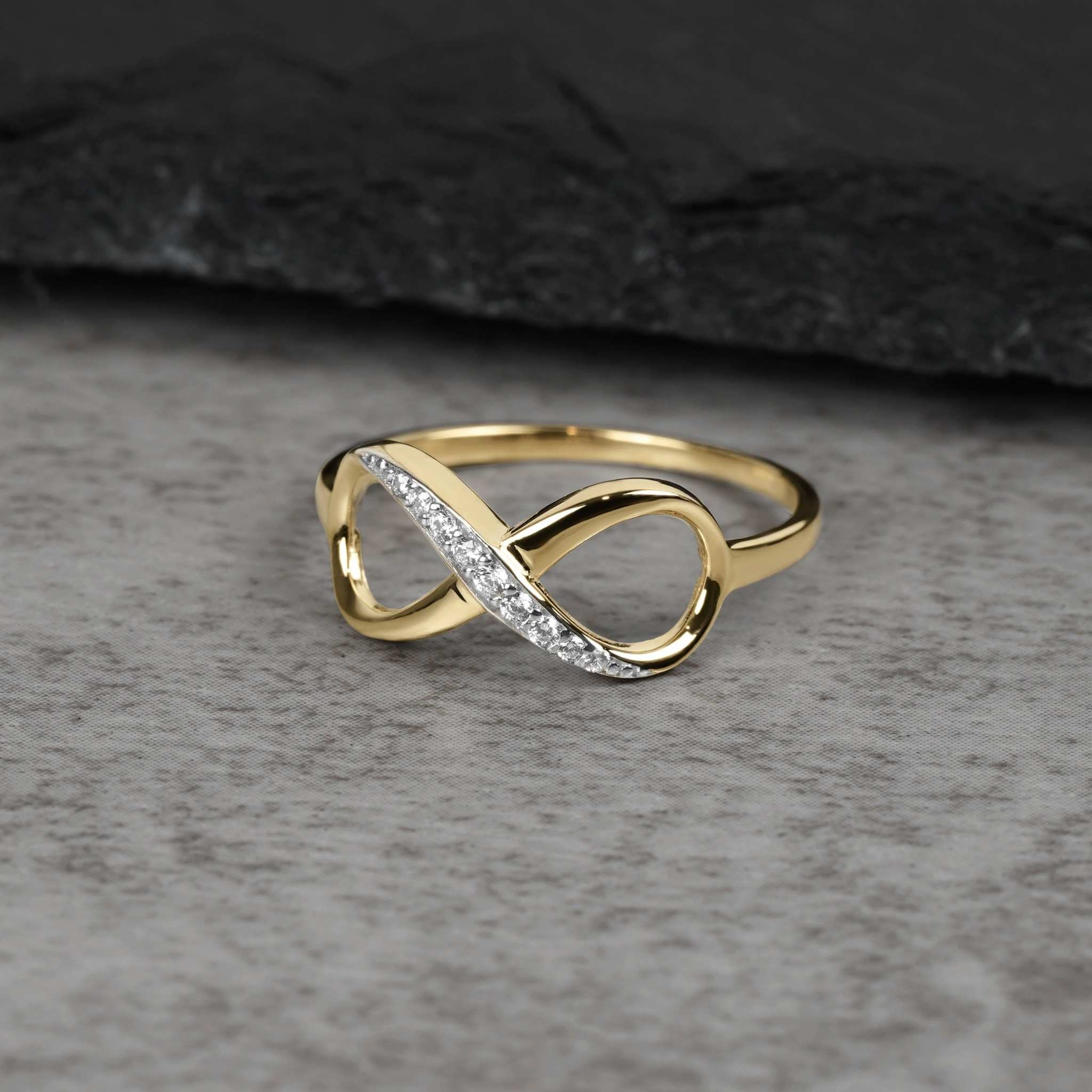 Solid yellow gold Meir infinity ring with cubic zirconia stones on gray stone surface.