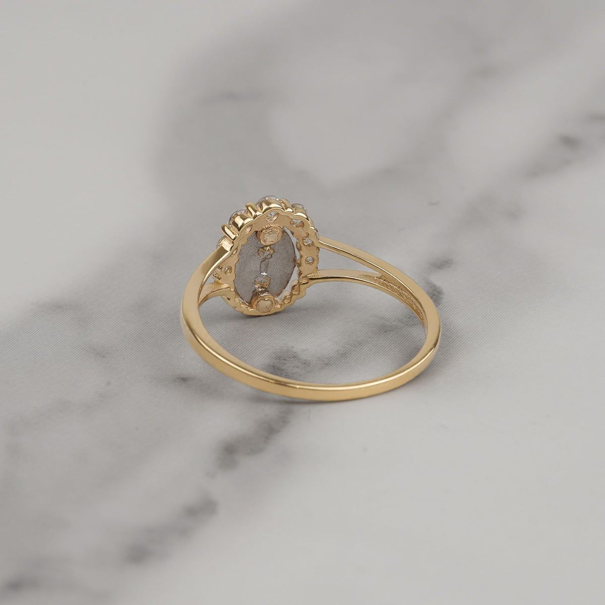 Back view of a gold Virgin Mary ring resting on white marble.