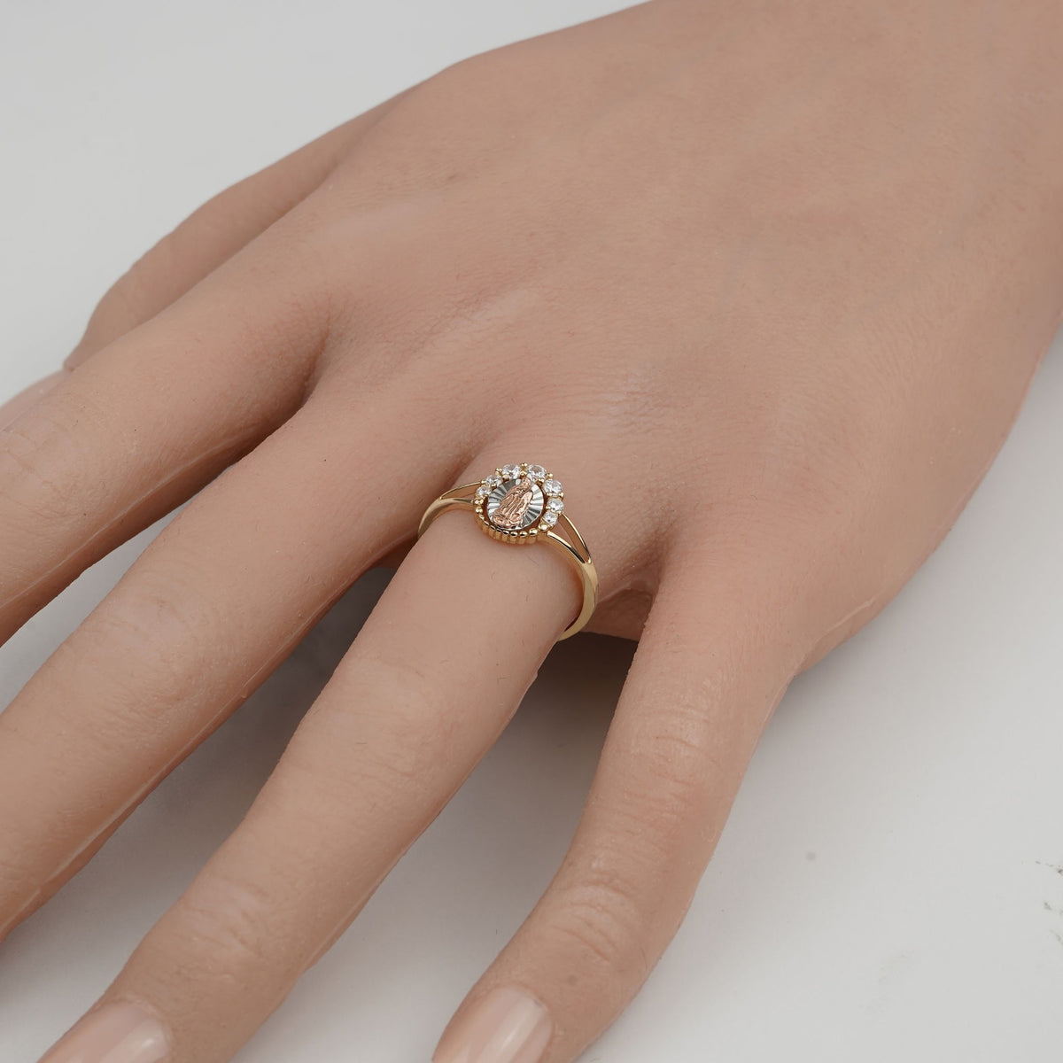 Dainty gold Virgin Mary ring worn on a finger against a plain background.