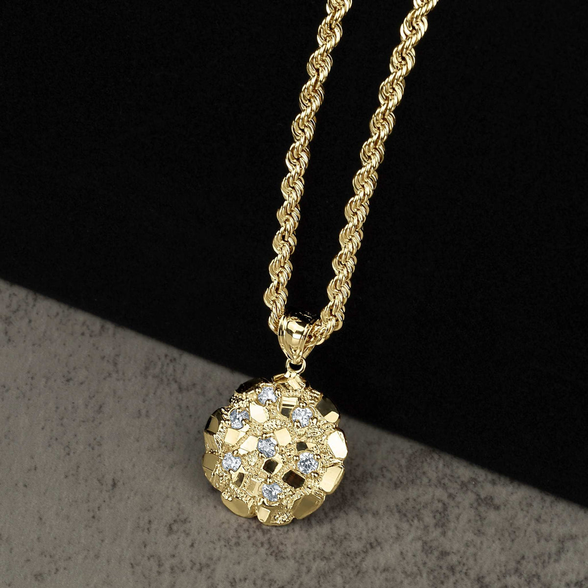 Gold rope chain necklace featuring a textured round nugget pendant with clear gemstones on a dark background.