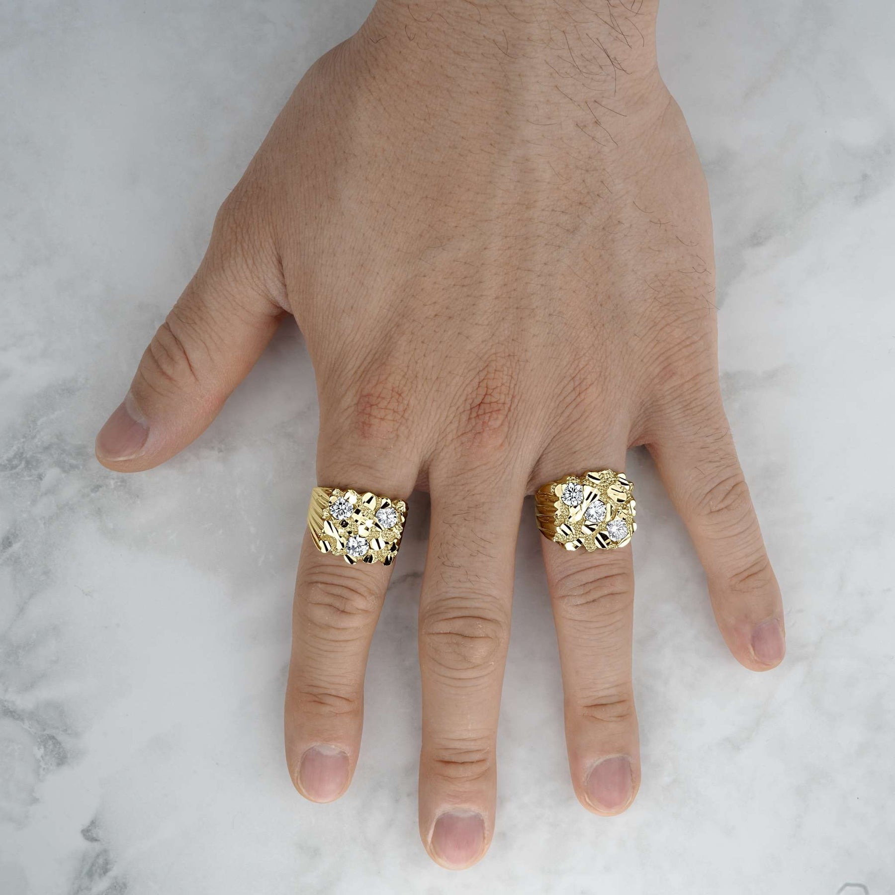 Two bold, textured yellow gold nugget rings with glittering gemstone accents displayed on a hand.