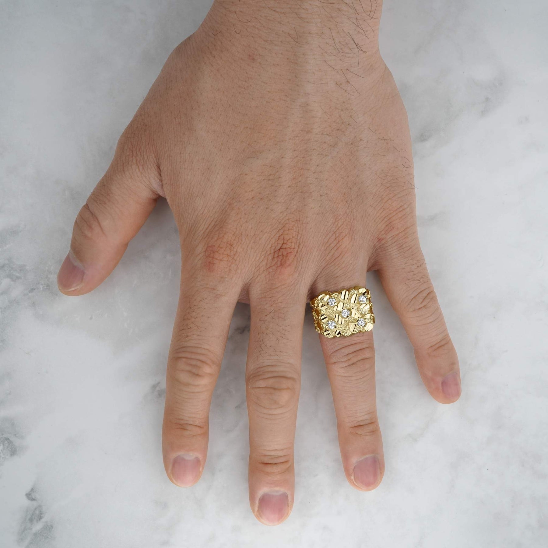 Close-up of a hand wearing a thick gold square cubic zirconia nugget ring over marble.