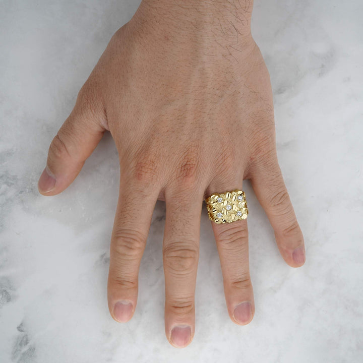 Close-up of a hand wearing a thick gold square cubic zirconia nugget ring over marble.