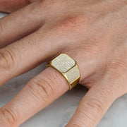 Detailed view of a gold square signet ring with cubic zirconia worn on a finger.