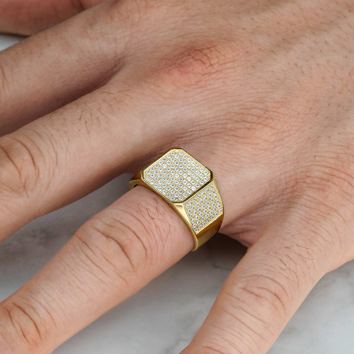 Detailed view of a gold square signet ring with cubic zirconia worn on a finger.