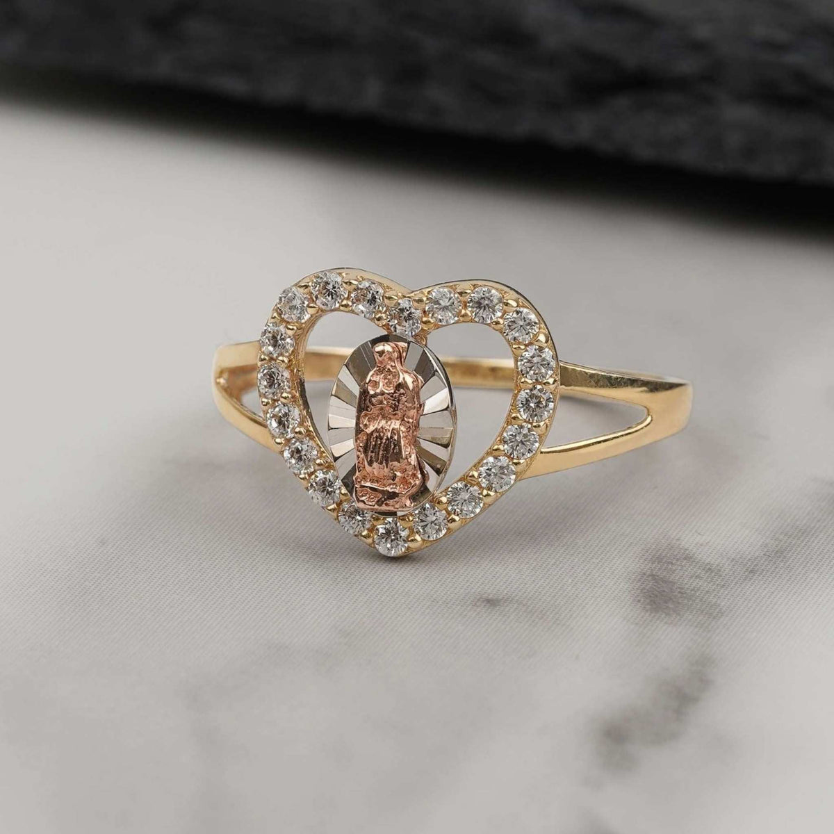 Gold heart ring featuring a rose gold Virgin Mary emblem surrounded by clear CZ stones.
