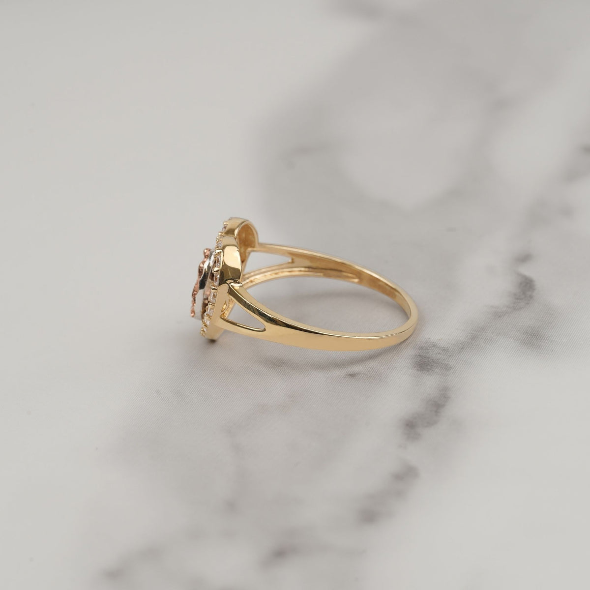 Side view of a gold Virgin Mary heart ring resting on white marble.