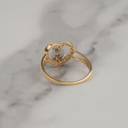 Back view of a gold Virgin Mary heart ring on white marble.