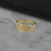 Polished yellow gold Orin lucky motif ring resting on a textured dark surface.