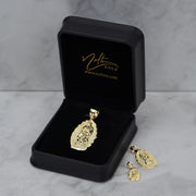 Gold religious pendant and matching earrings presented in an open black 'Nolters' jewelry box.