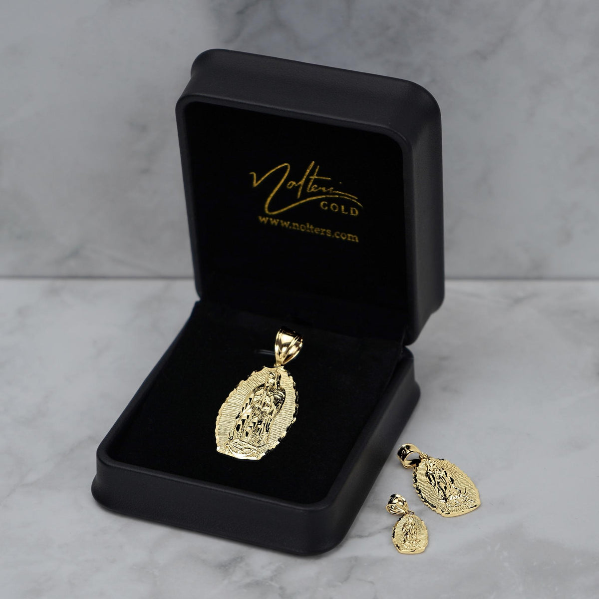 Gold religious pendant and matching earrings presented in an open black 'Nolters' jewelry box.
