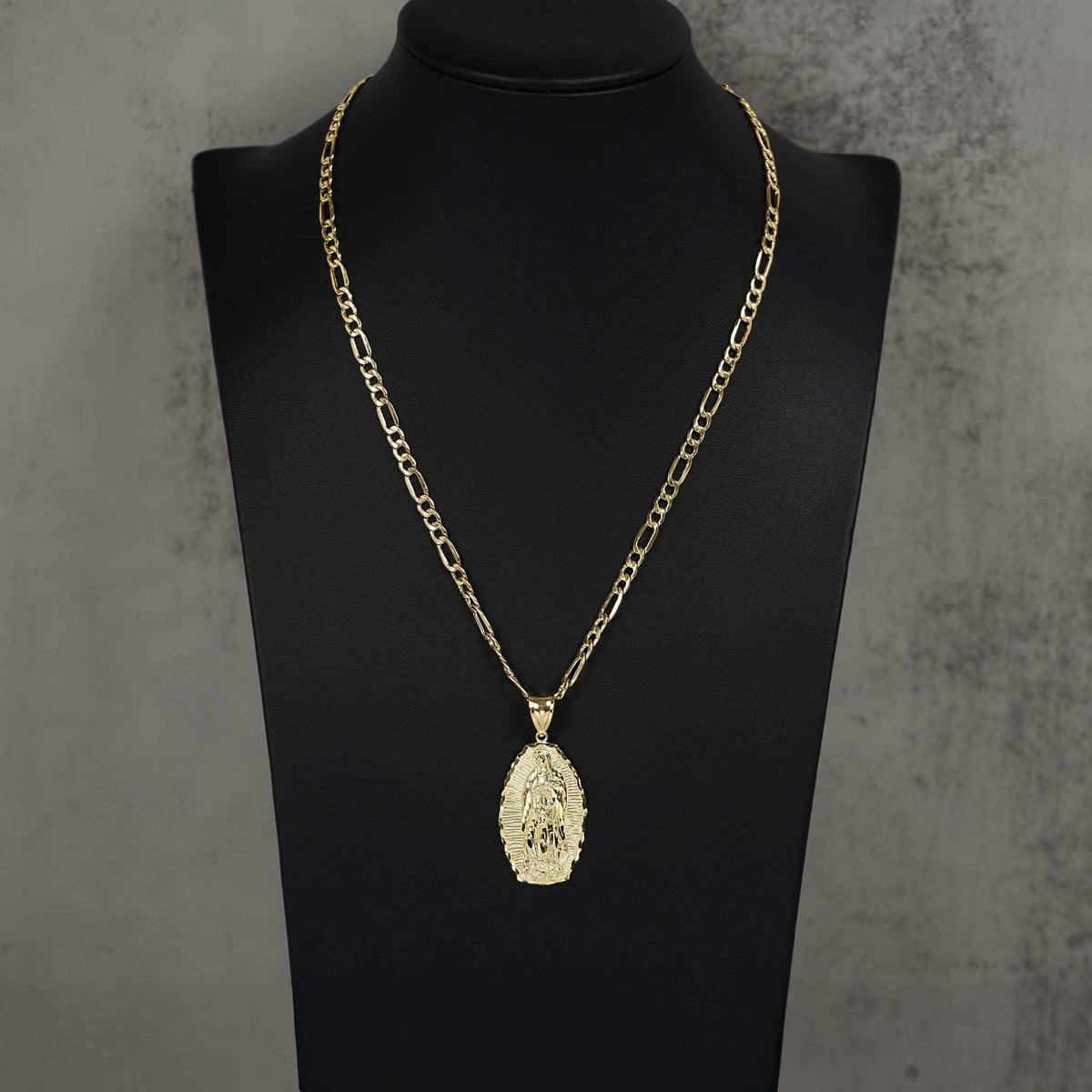 Gold chain necklace with an oval Guadalupe pendant displayed on a black jewelry mannequin bust.