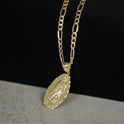 Gold Figaro chain with oval Guadalupe pendant, displayed on a black and gray background.