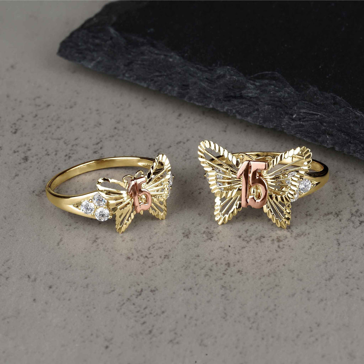 Two sizes of the gold two-tone classic butterfly Quinceañera ring on gray surface.
