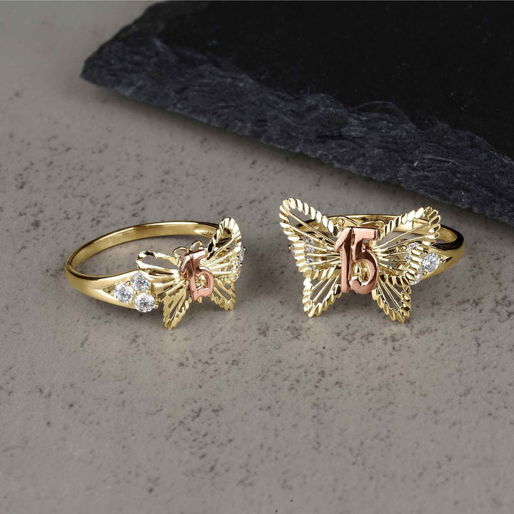 Two sizes of the gold two-tone classic butterfly Quinceañera ring on gray surface.