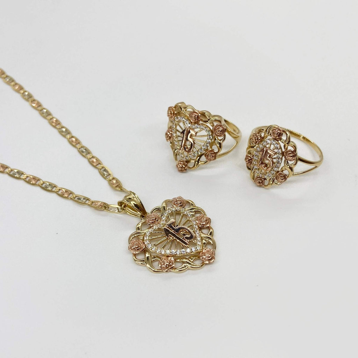 Gold necklace and two Quinceanera Bloom Rose heart shape rings on a light gray background