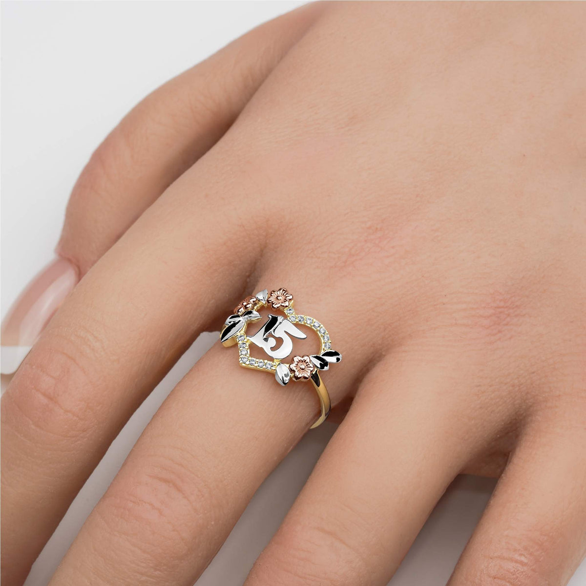 Model wearing a yellow gold ring with a tri-color number 15 heart design