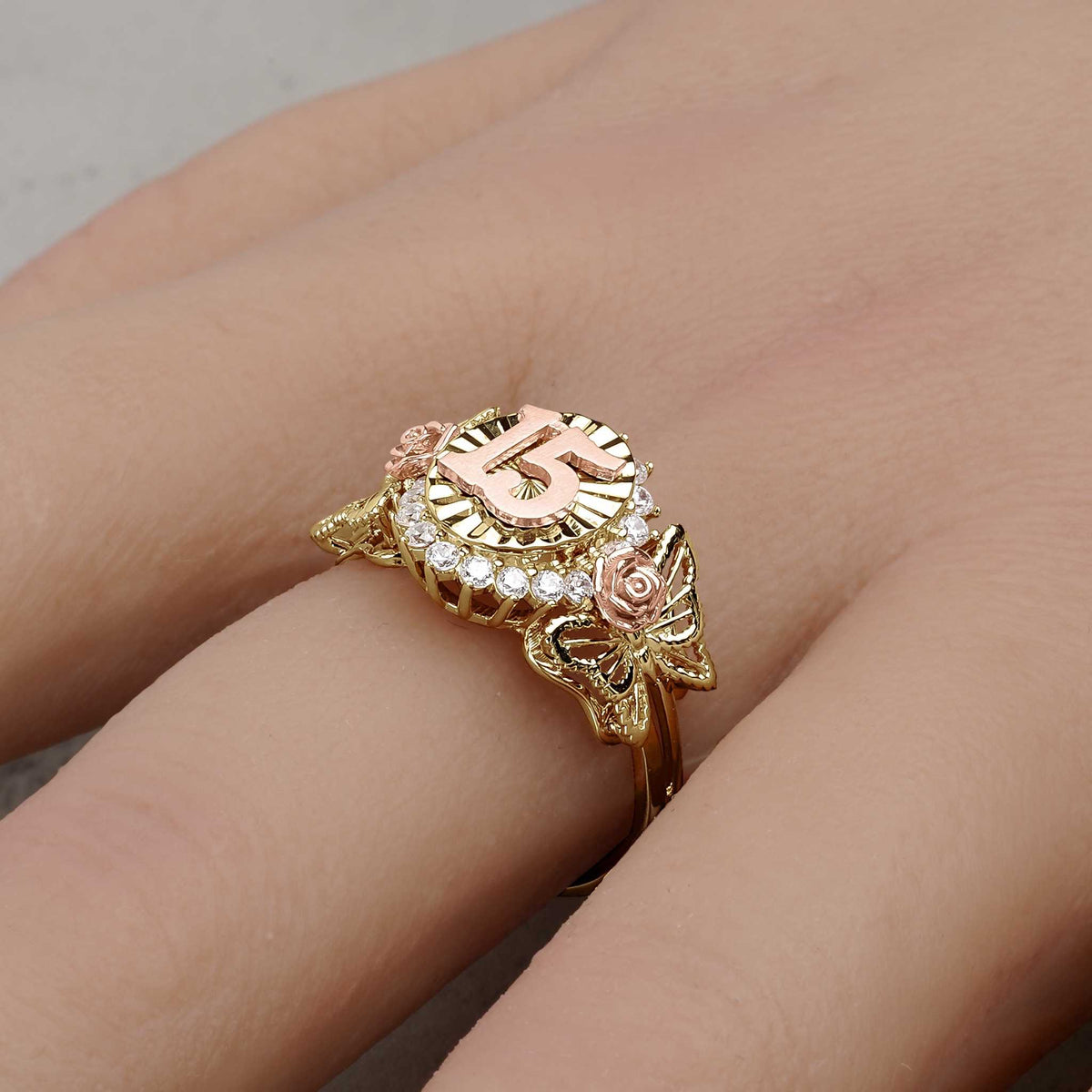 A gold two-tone Quinceañera 15 ring with rose details being worn on a finger.
