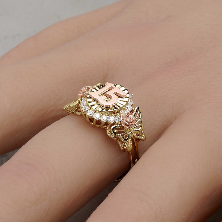 A gold two-tone Quinceañera 15 ring with rose details being worn on a finger.