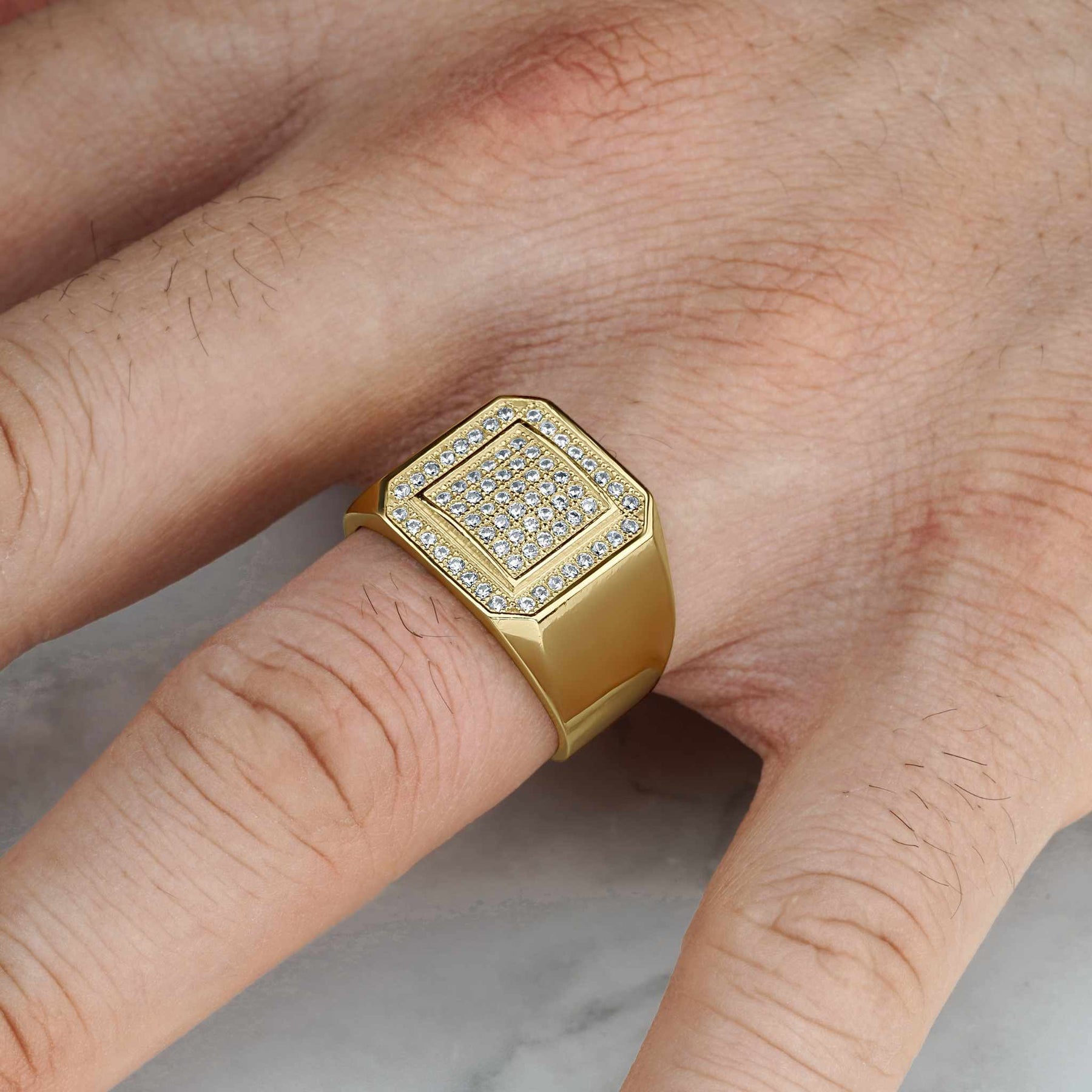 Gold square signet ring with glittering cubic zirconia worn on a person's hand.