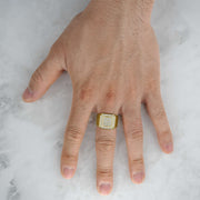 Gold square signet ring with glittering cubic zirconia on a hand over marble.