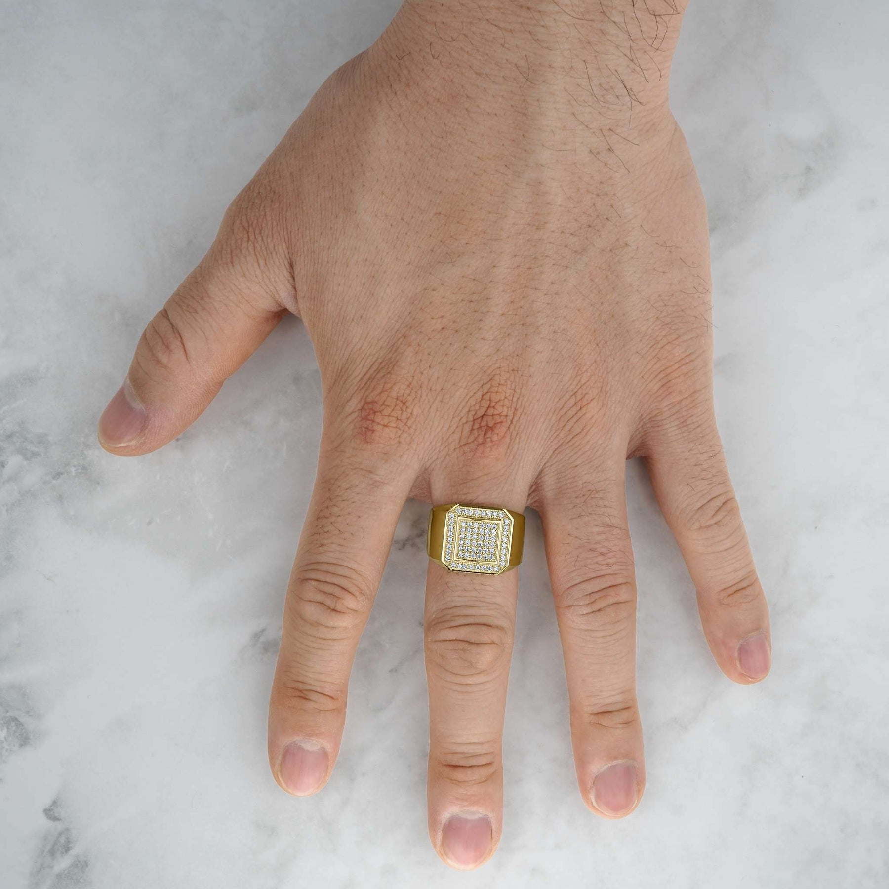 Gold square signet ring with glittering cubic zirconia on a hand over marble.