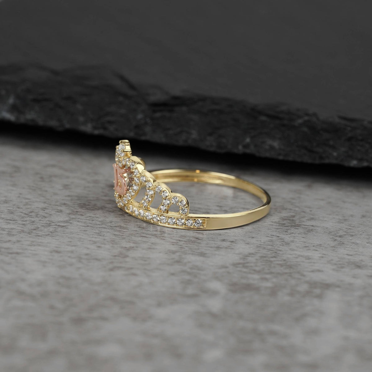 Side profile of a gold royal crown ring with CZ crystals on dark stone.