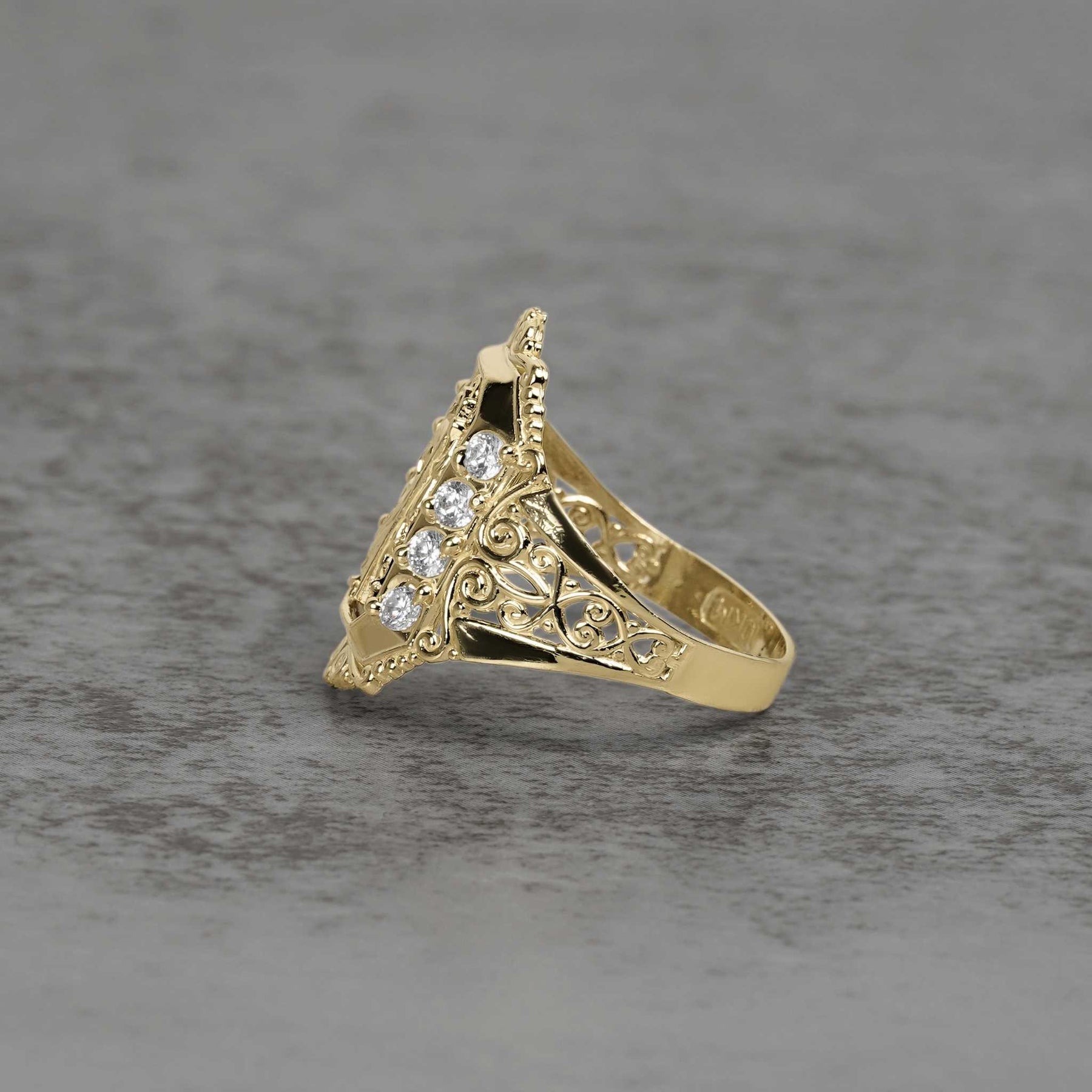 Side view of a two-tone gold San Judas ring with cubic zirconia on textured background.