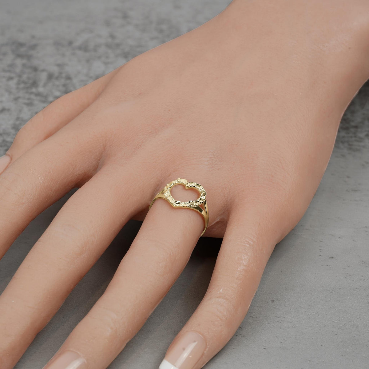 Hand wearing a 10k and 14k gold open-heart nugget ring on a textured background.