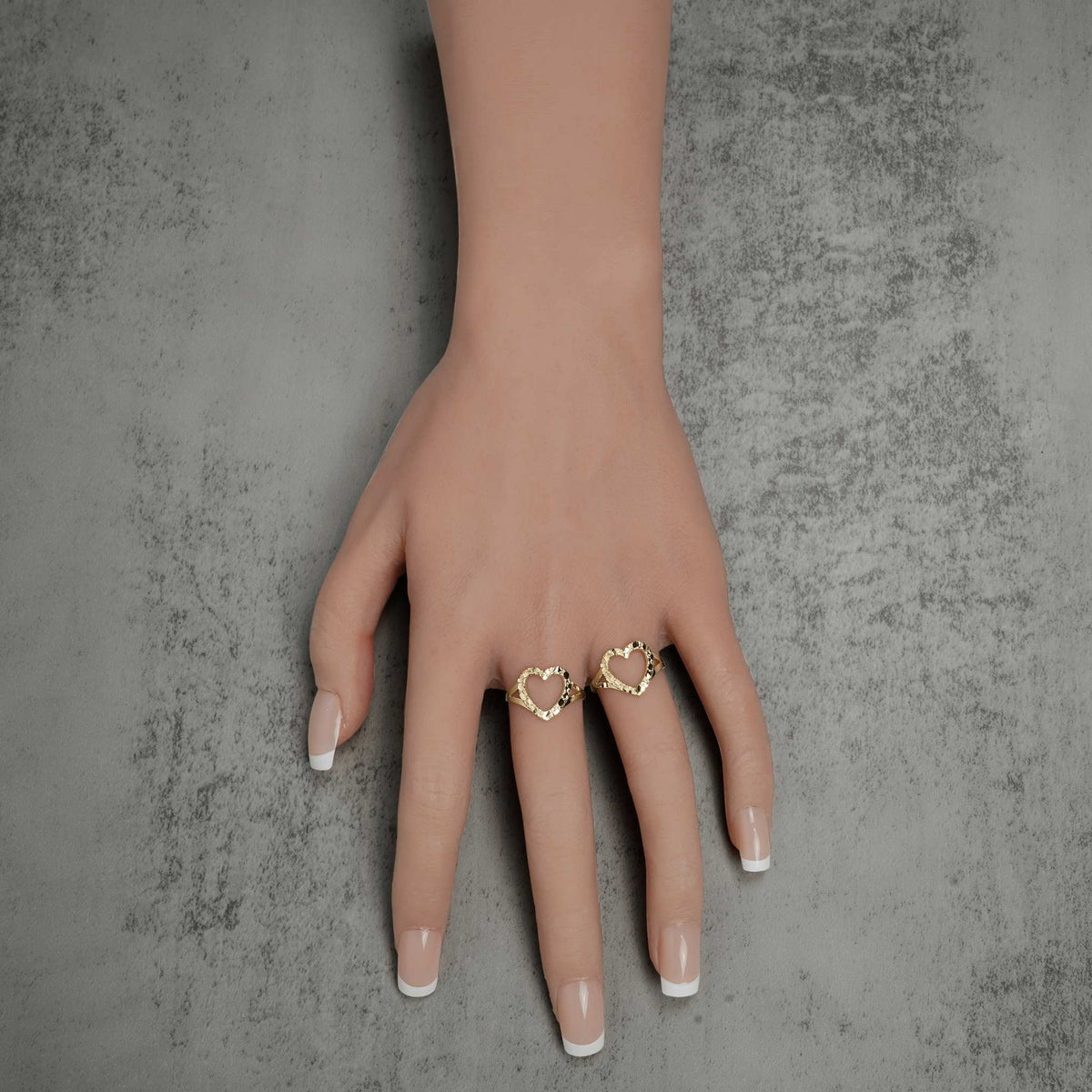 Two 10k and 14k gold open-heart nugget rings worn on a hand against a gray background.