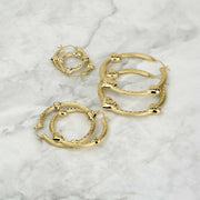 Three different sizes of textured gold tre heart hoop earrings on a marble surface.