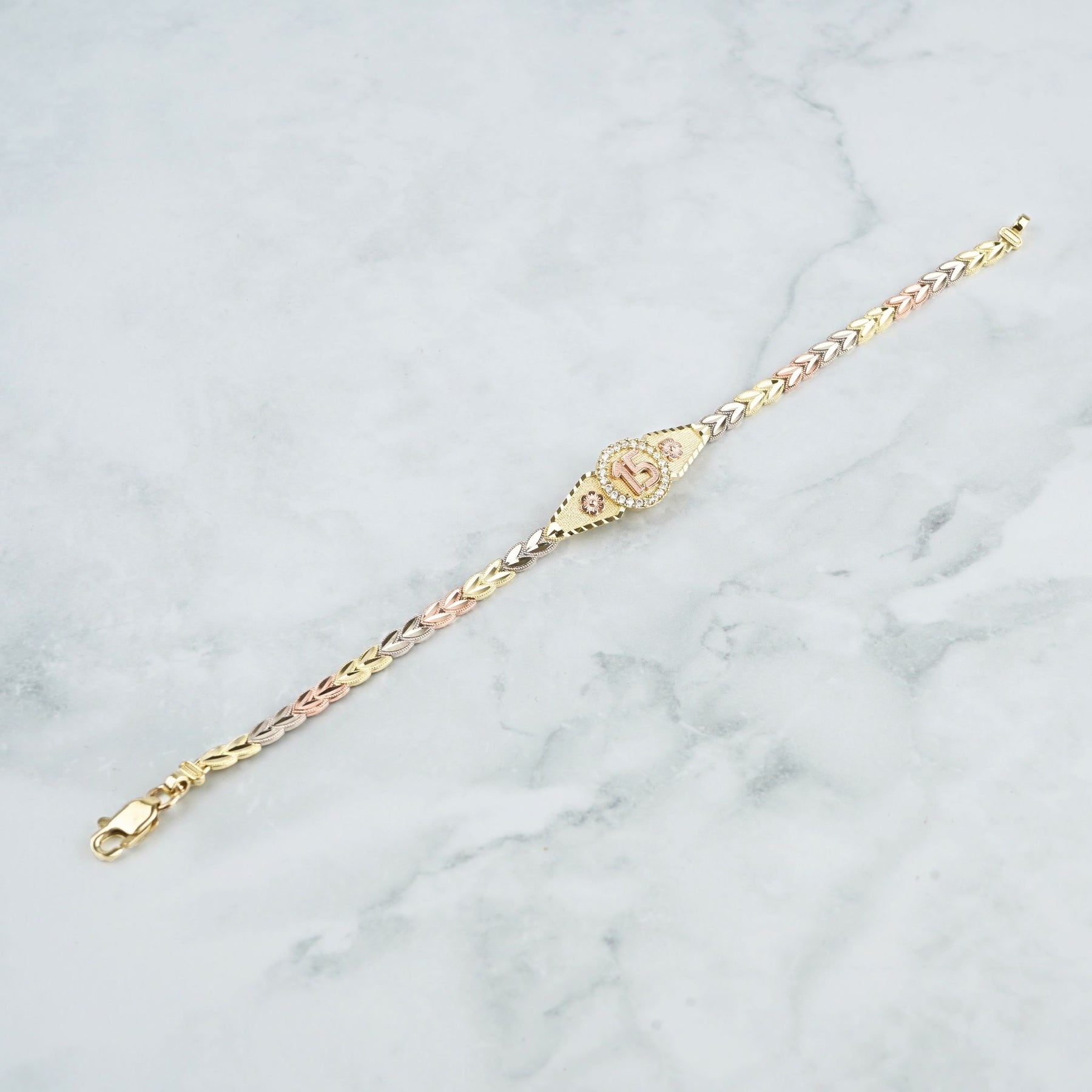 Delicate tri-color gold leaf bracelet featuring a pavé-set "15 Anos" center charm.